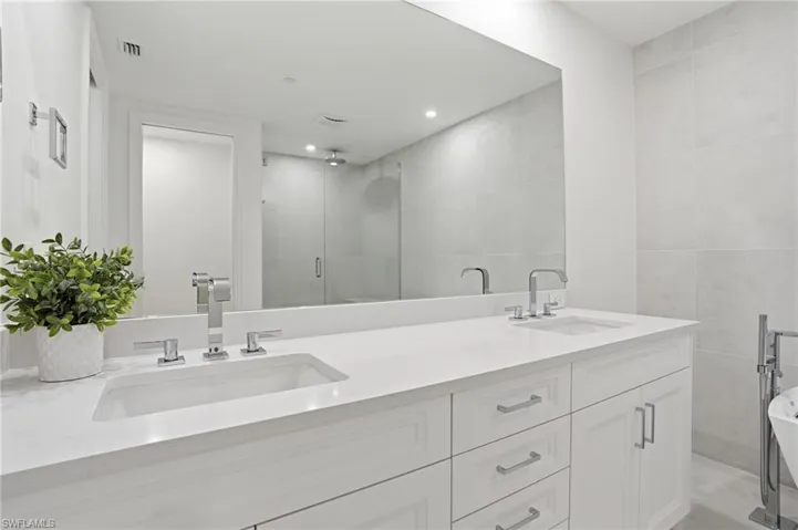 Dual vanity with integrated sinks, chrome fixtures, built-in cabinetry, and a full-width mirror