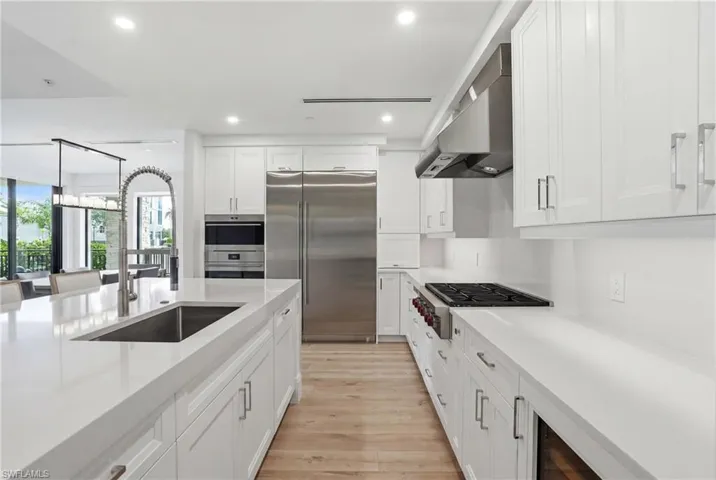 Gourmet kitchen with white cabinetry, stainless steel appliances, a large island with an undermount sink, and wood-finish flooring