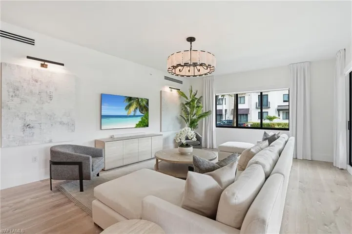Recessed ceiling lighting, wood-finish flooring, built-in media console, large windows, and a decorative chandelier