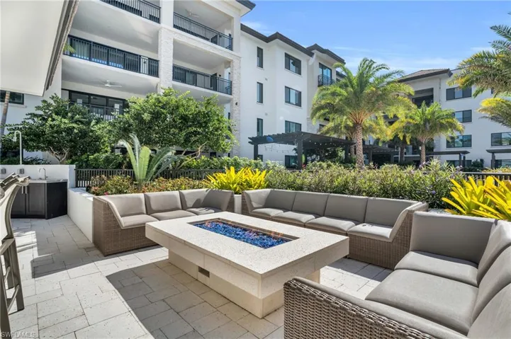 Paved patio featuring a built-in fire pit, outdoor kitchen area, and lush landscaping