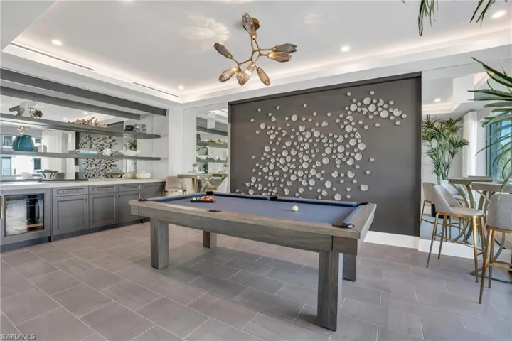 Recessed ceiling lighting, a contemporary chandelier, a built-in wet bar with mirrored backsplashes, open shelving, and neutral tone tile flooring