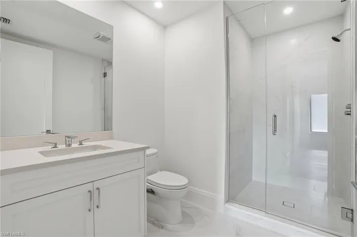 Integrated vanity with dual-handle faucet, frameless glass shower enclosure, recessed lighting, and large format floor tiling