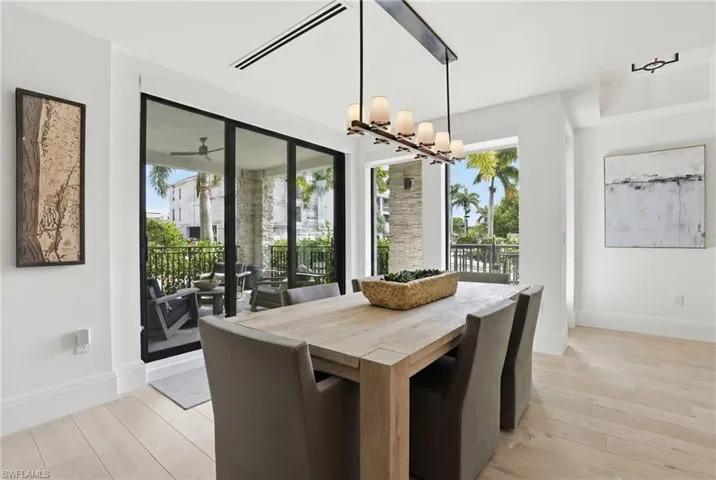 Light wood-finish flooring, white walls, and a contemporary linear chandelier illuminate this dining area