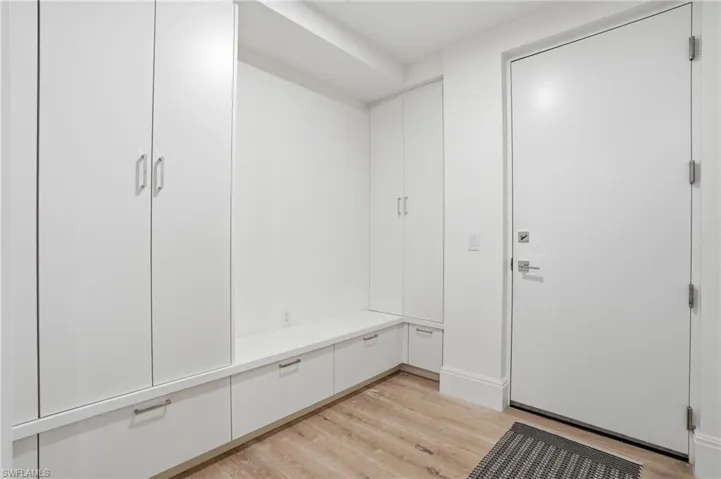 Built-in storage cabinetry with integrated seating and contemporary hardware, light wood-finish flooring, and a solid entry door with modern fixtures