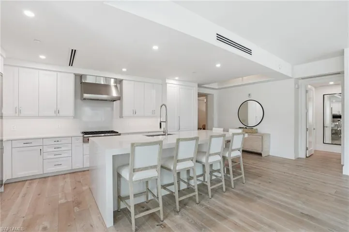 Gourmet kitchen with white cabinetry, stainless steel range hood, stone countertops, and a waterfall island