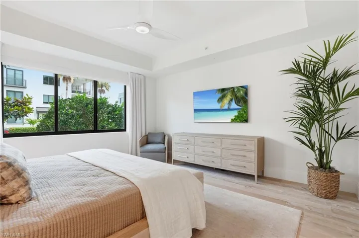 Recessed ceiling, tray ceiling, window with dark framing, wood-finish flooring, ceiling fan with integrated lighting