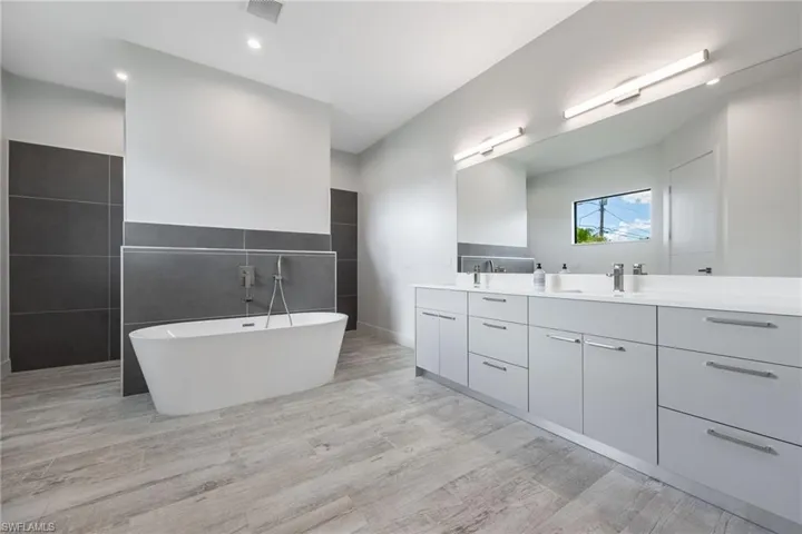 Full bath featuring double vanity, a freestanding tub, wood finished floors, tile walls, and recessed lighting
