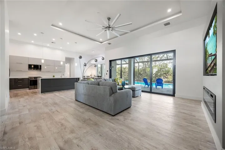 Living area featuring a high ceiling, recessed lighting, light wood finished floors, a raised ceiling, and a ceiling fan