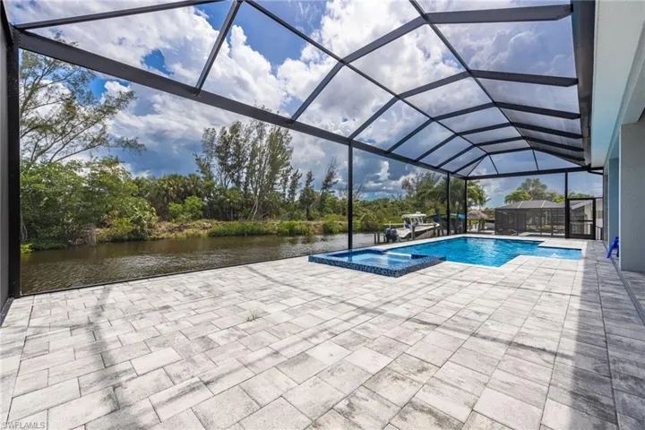 View of pool featuring a patio area, a water view, glass enclosure, and a pool with connected hot tub