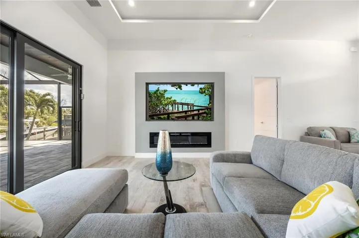 Living area with wood finished floors, a raised ceiling, a glass covered fireplace, and recessed lighting