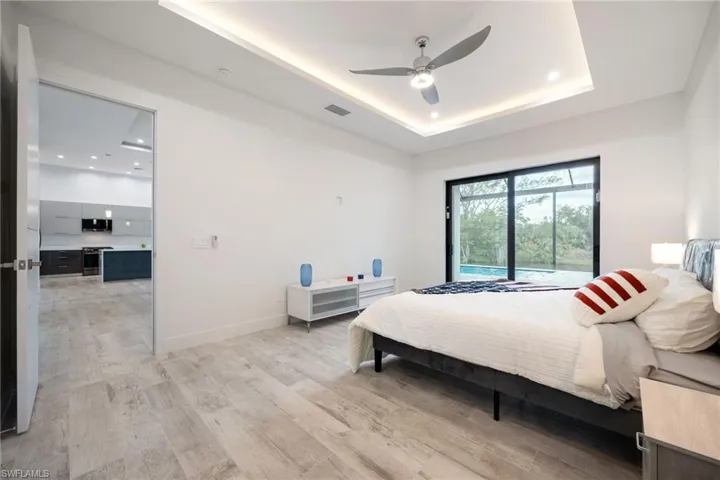 Bedroom with light wood-style flooring, ceiling fan, recessed lighting, and a tray ceiling