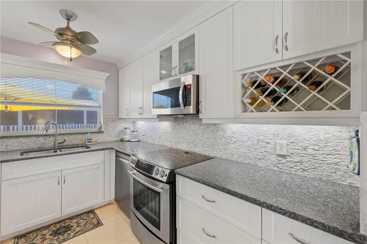 Kitchen with ceiling fan, white cabinetry, backsplash, stainless steel appliances, and sink