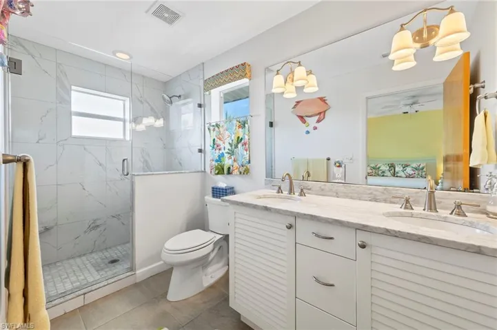 Bathroom featuring a shower with door, a healthy amount of sunlight, double vanity, and toilet