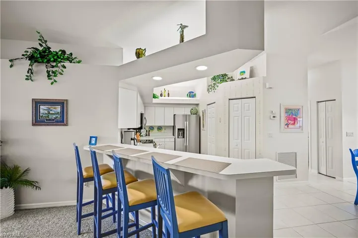 Kitchen with kitchen peninsula, a breakfast bar area, light tile patterned floors, stainless steel fridge with ice dispenser, and white cabinetry