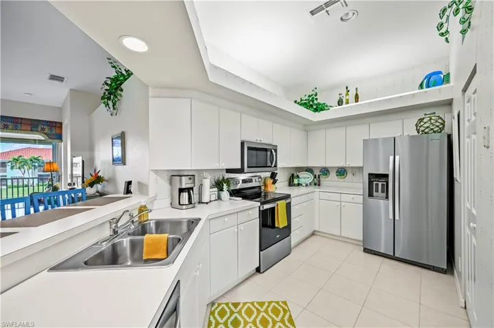 Kitchen with stainless steel appliances, white cabinets, decorative backsplash, sink, and light tile patterned floors