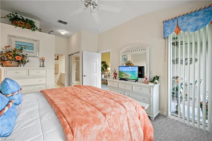 Carpeted bedroom with ensuite bath, ceiling fan, and vaulted ceiling