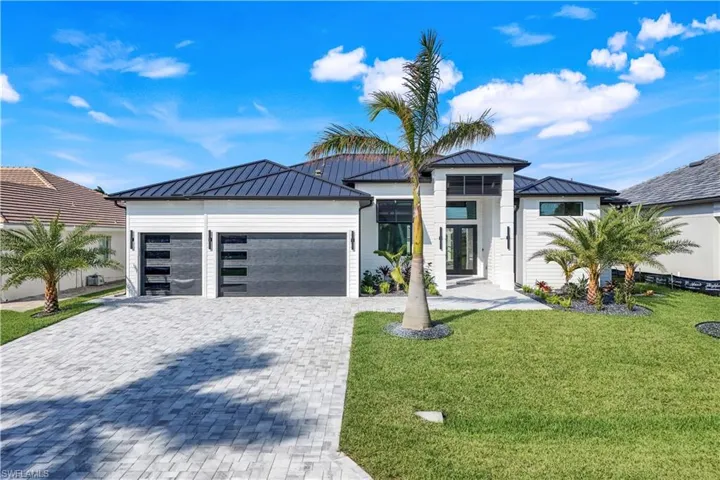 Modern home with metal roof, decorative driveway, a garage, a standing seam roof, and a front lawn