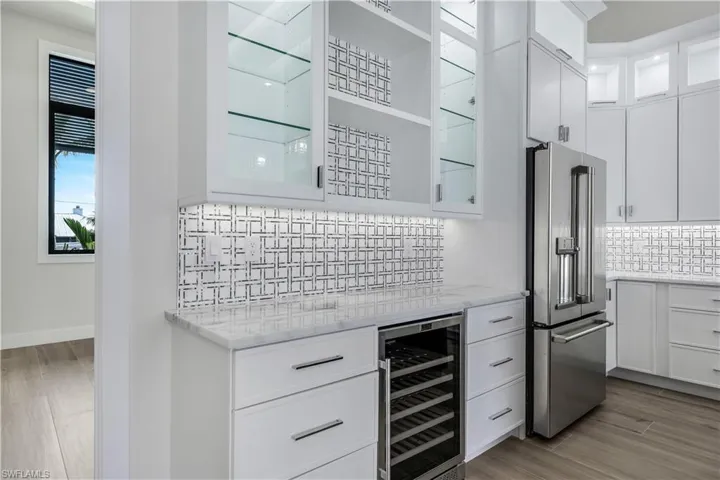 Kitchen featuring beverage cooler, high end fridge, decorative backsplash, and white cabinetry