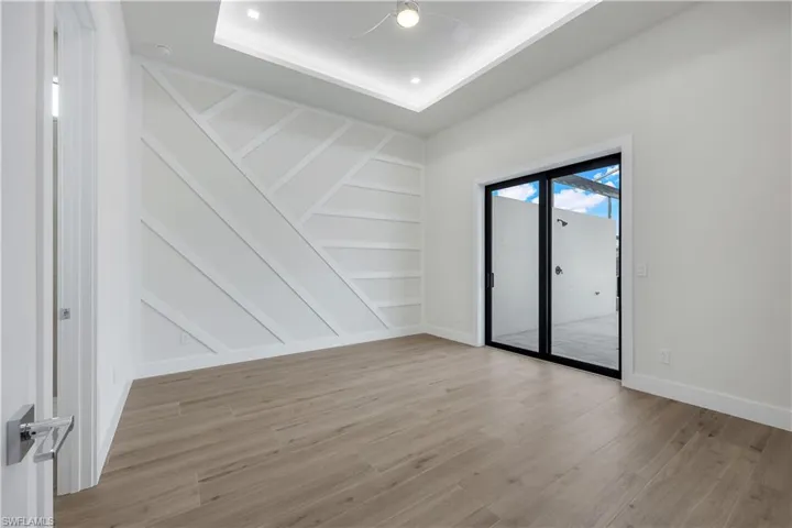 Empty room with a tray ceiling, baseboards, light wood finished floors, and built in shelves