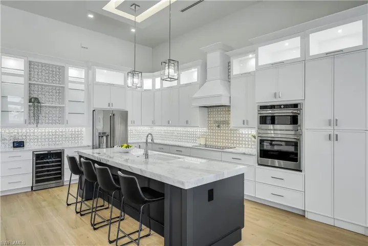 Kitchen featuring wine cooler, appliances with stainless steel finishes, decorative backsplash, white cabinets, and an island with sink