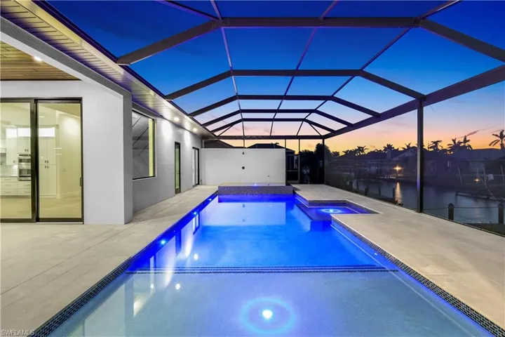 View of pool featuring a pool with connected hot tub, a water view, glass enclosure, and a patio