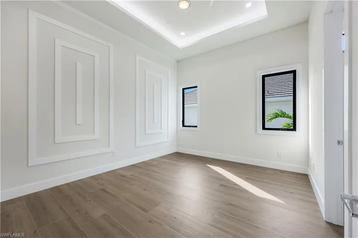 Spare room featuring a tray ceiling, baseboards, and wood finished floors