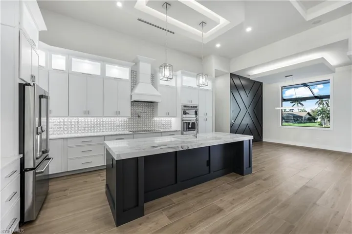 Kitchen featuring tasteful backsplash, appliances with stainless steel finishes, a center island with sink, light wood-type flooring, and custom exhaust hood