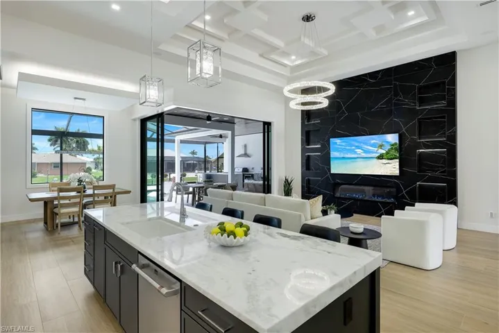 Kitchen with dark cabinetry, open floor plan, stainless steel dishwasher, hanging light fixtures, and light stone counters