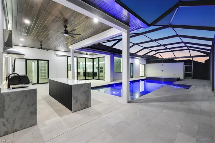 Pool with area for grilling, a patio, glass enclosure, a sink, and a hot tub