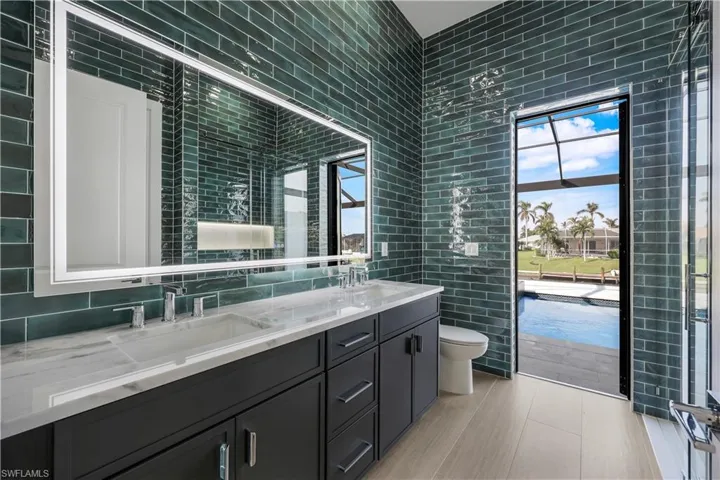 Bathroom with toilet, double vanity, a sink, and tile walls