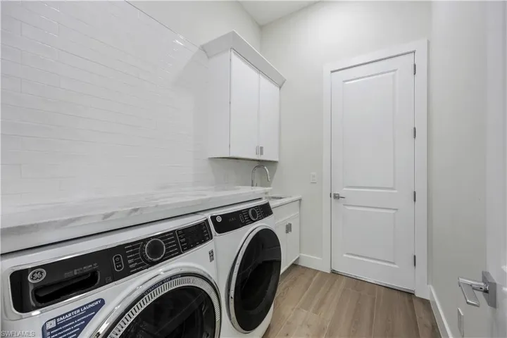 Washroom with a sink, light wood finished floors, washing machine and clothes dryer, baseboards, and cabinet space