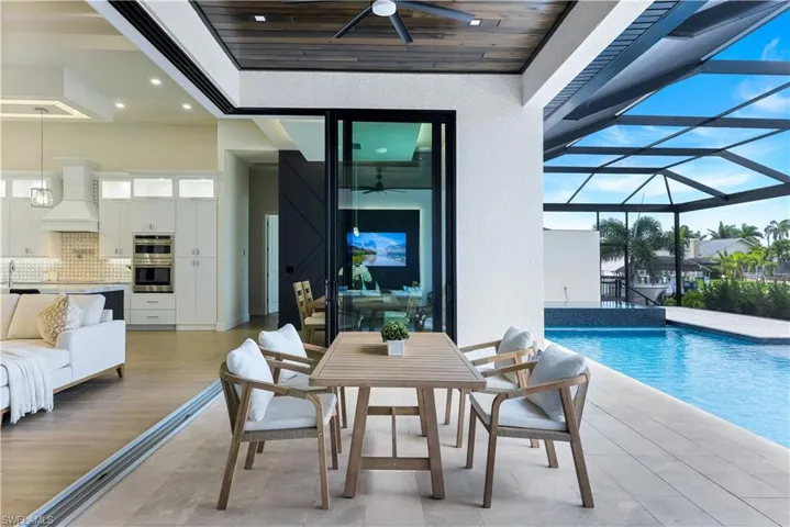 View of swimming pool featuring a ceiling fan, glass enclosure, area for grilling, a pool with connected hot tub, and a patio