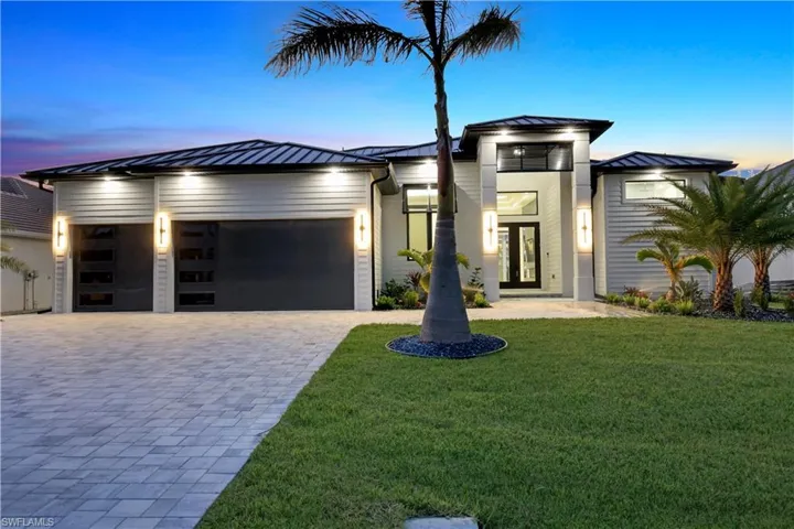Modern home featuring metal roof, decorative driveway, an attached garage, a standing seam roof, and a front lawn