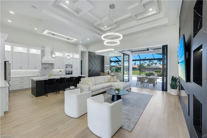 Living room featuring a towering ceiling, light wood-style floors, coffered ceiling, beam ceiling, and a chandelier