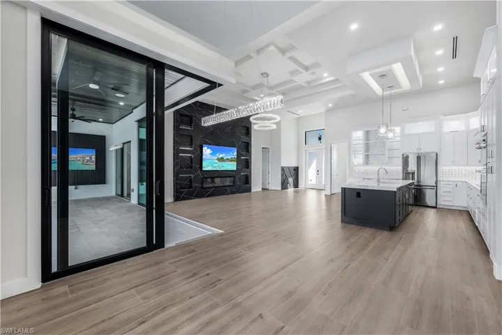 Unfurnished living room featuring coffered ceiling, a notable chandelier, light wood finished floors, a high ceiling, and recessed lighting