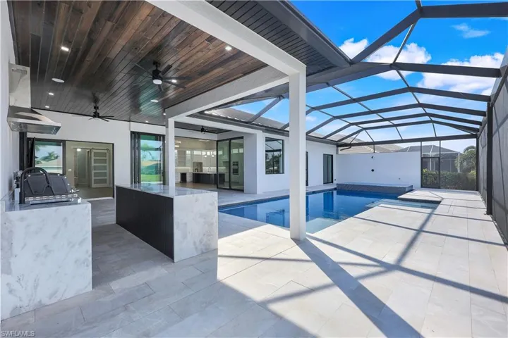 Pool featuring a ceiling fan, an outdoor kitchen, glass enclosure, and a patio area