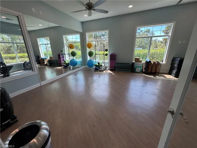 Spacious fitness area featuring wood-finish flooring, ample natural light from multiple large windows, full-wall mirrors, recessed lighting, and a ceiling fan