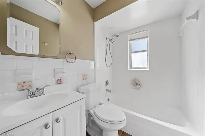 Full bathroom with bathing tub / shower combination, vanity, tile walls, and a wainscoted wall