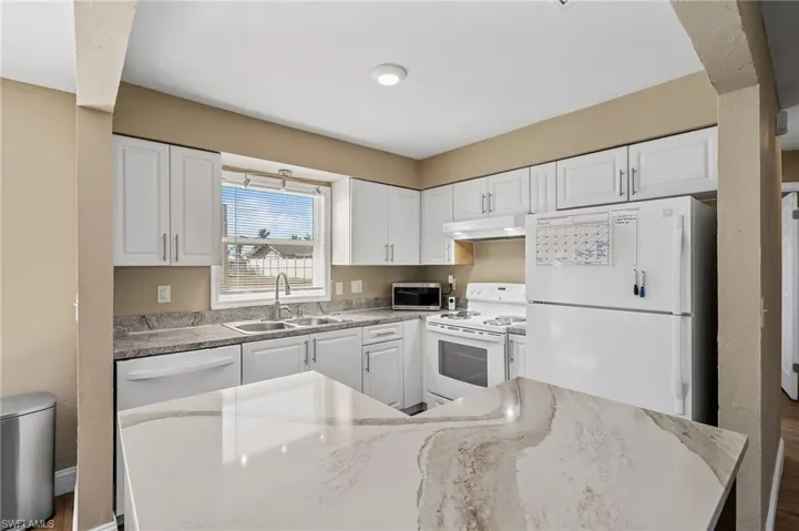 Kitchen with white appliances, white cabinets, under cabinet range hood, and light stone counters