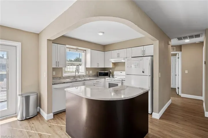 Kitchen featuring white appliances, white cabinetry, a center island, and light wood-type flooring