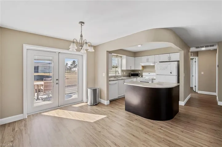 Kitchen with white cabinetry, decorative light fixtures, white appliances, and light wood-type flooring