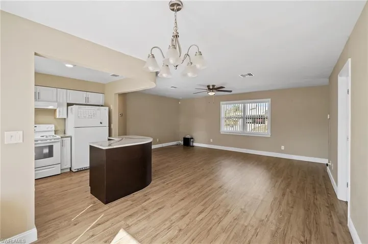 Kitchen with decorative light fixtures, white appliances, open floor plan, and light wood-style flooring