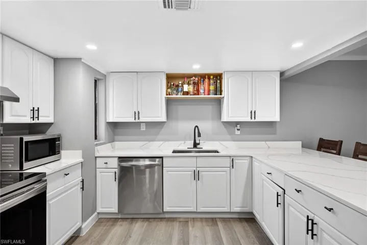 Kitchen featuring white cabinetry, light stone countertops, stainless steel appliances, light wood finished floors, and recessed lighting