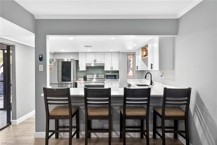 Kitchen with white cabinets, stainless steel appliances, a kitchen bar, a peninsula, and light wood-style flooring