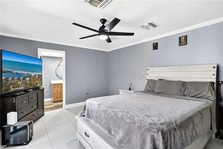 Primary Bedroom 2 featuring crown molding, ensuite bath, light marble finish floors, and a ceiling fan