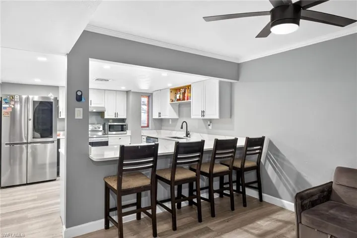 Kitchen featuring stainless steel appliances, light wood-style floors, white cabinets, crown molding, and a peninsula