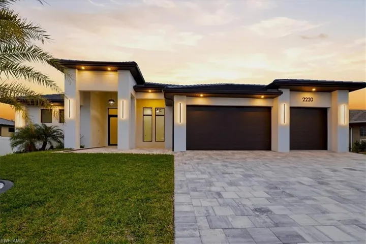 View of front of property with an attached garage, a lawn, decorative driveway, stucco siding, and a tile roof