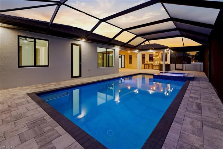 Pool at dusk with a sunroom, a lanai, a pool with connected hot tub, and a patio area