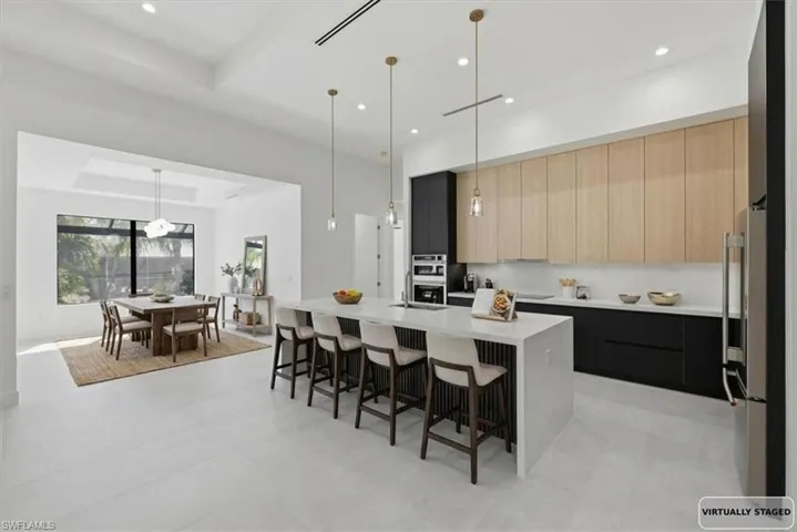 Two tone kitchen featuring a raised ceiling, an island with sink, light stone counters, a kitchen bar, and modern cabinets
