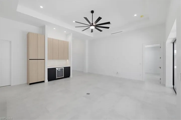 Unfurnished living room with beverage cooler, a raised ceiling, ceiling fan, and recessed lighting